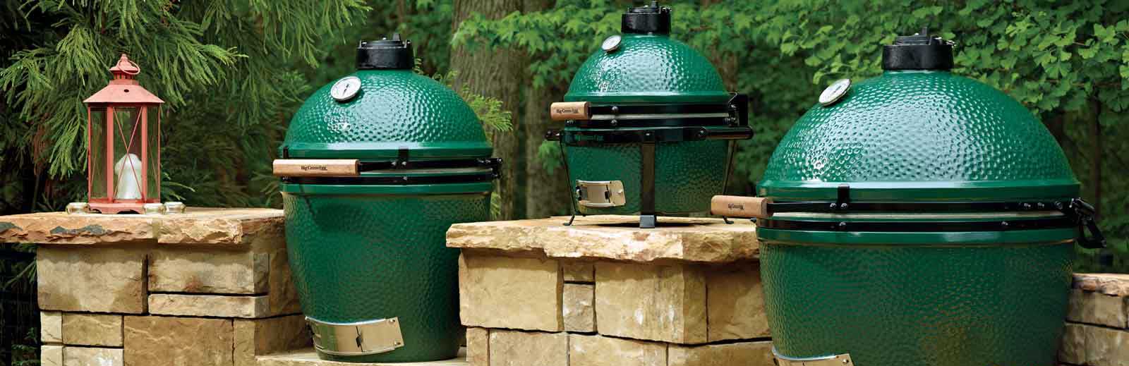 Three Green Egg Smokers sitting on Stone Columns on patio with red lantern to the side and lush greenery in the background