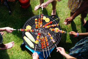 people holding skewers of meats and veggies over charcoal grill 